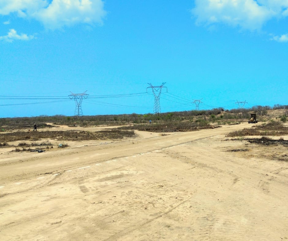 Vista panorámica a nivel de suelo del predio, camino de terracería y torres de transmisión al fondo